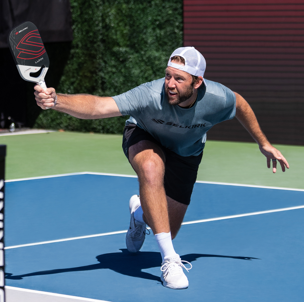 A player lunging to hit a pickleball with a Selkirk paddle on a court.