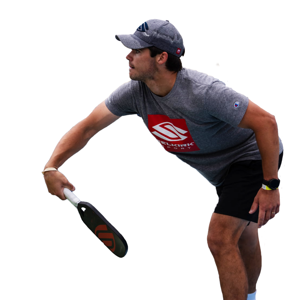 Athlete reaching to hit a pickleball with paddle, wearing a gray SELKIRK SPORT shirt