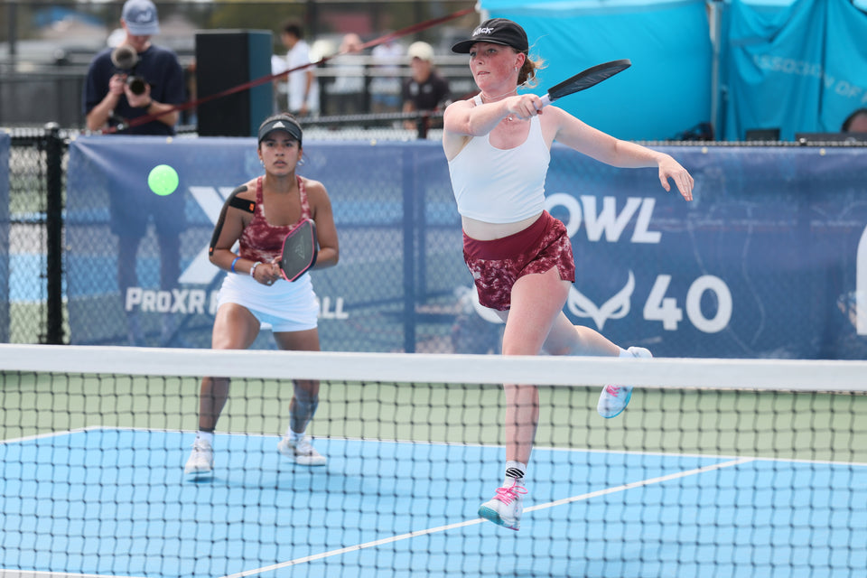 Two women playing pickleball at the net, one lunging to hit the ball; banners behind read 'PROXR' and 'OWL 40'
