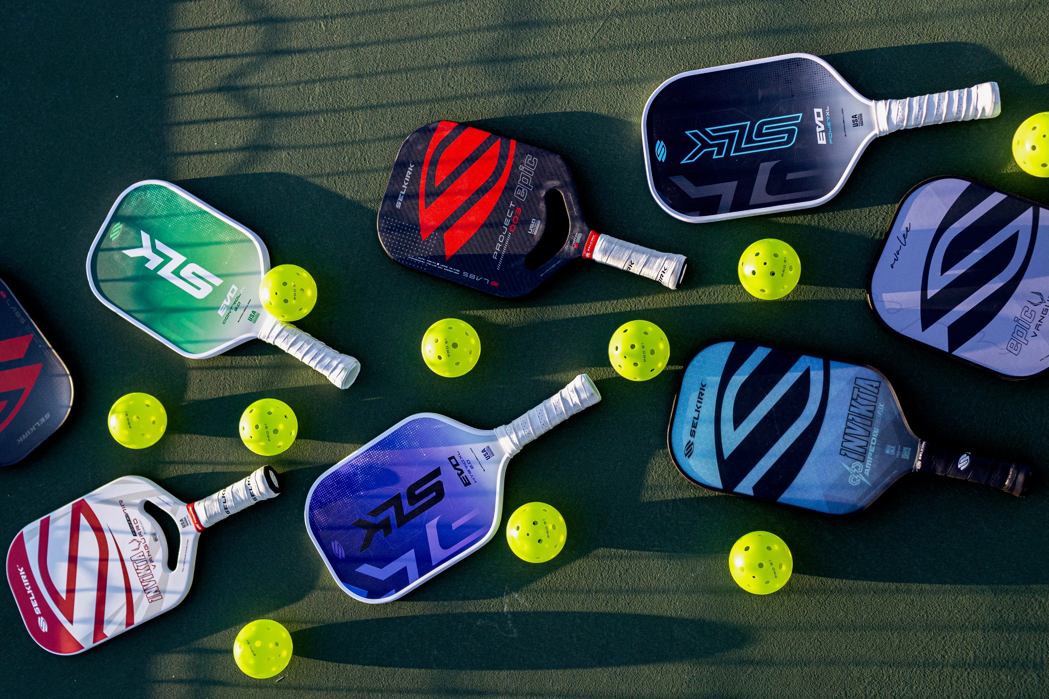 Various pickleball paddles in different colors and designs on a court with yellow balls.