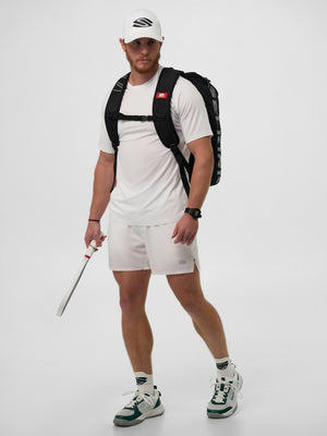 Male model in white tennis kit and cap, green-accent sneakers, black backpack, holding a white tennis racket