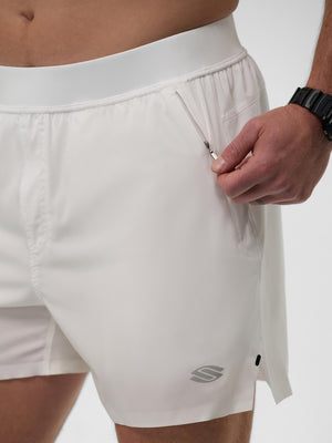 White men's athletic shorts with side zipper pocket being opened by a hand wearing a black watch; reflective logo on hem.