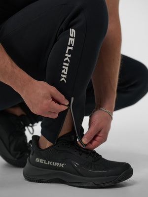 Man adjusting zippered ankle of Selkirk Pro Line Knit Jogger, showing logo on pants and shoes.