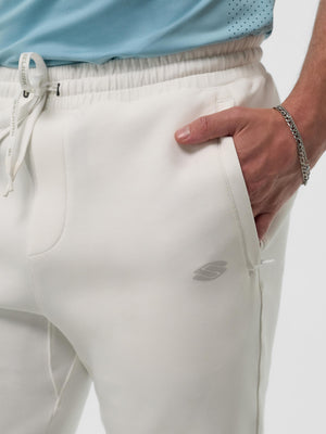 Off-white Skechers joggers with elastic drawstring waist, left hand in pocket; visible 'S' logo and SKECHERS on drawstring.