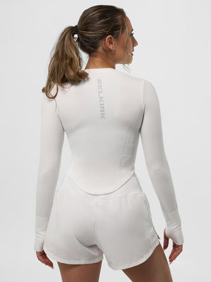 Female model shown from back wearing white long-sleeve athletic top and shorts, SELKIRK logo printed vertically on upper back.
