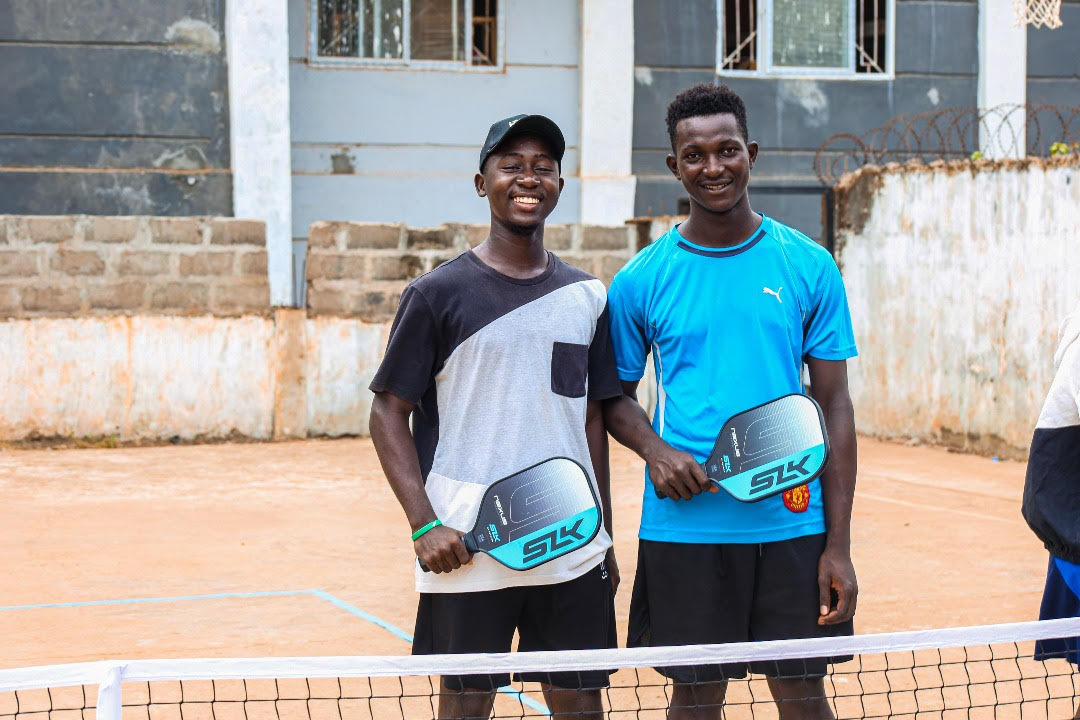 Two boys smiling on a dirt pickleball court holding SLK Nexus paddles.