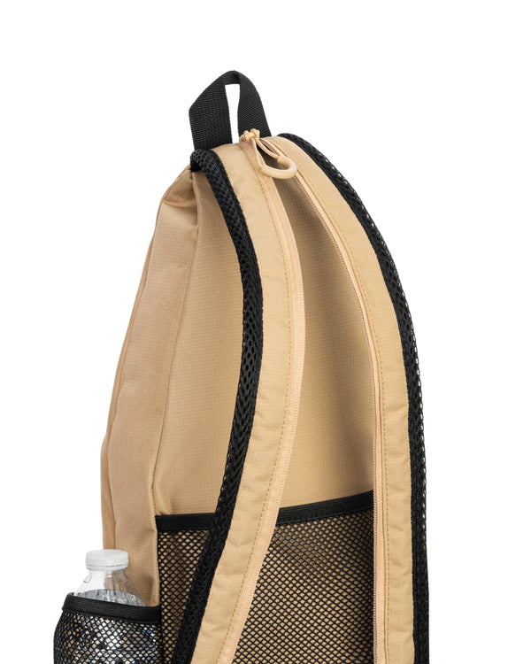 Beige sling backpack side view with mesh water-bottle pocket and black-trimmed shoulder strap