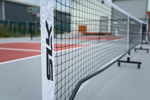 Close-up of an outdoor tennis net and white post branded 'STK' on a court.