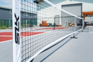 Close-up of a court net and white post with SZK logo on an outdoor pickleball/tennis court.