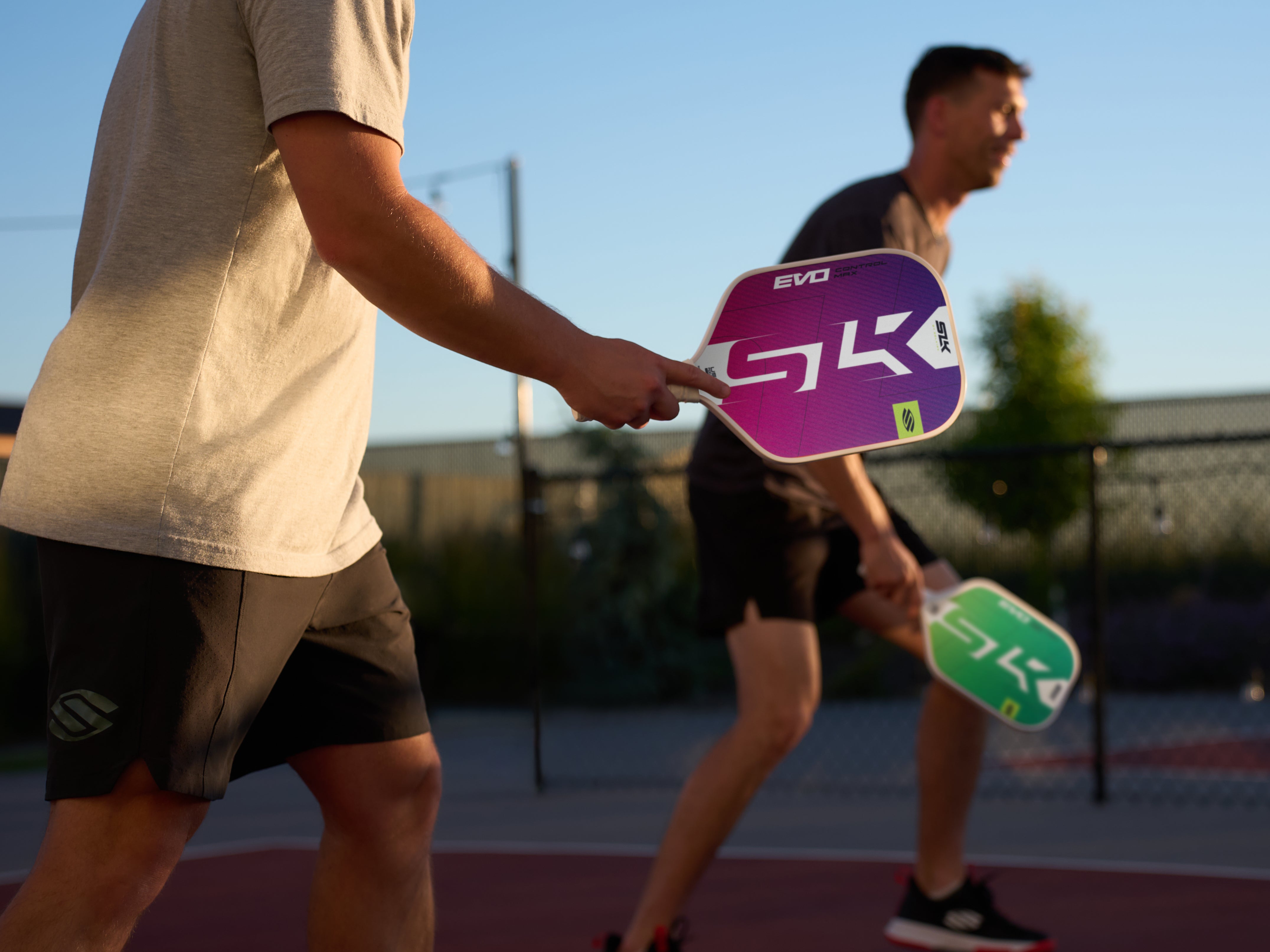 Two players on a court holding SLK Latitude and SLK EVO paddles during a game.