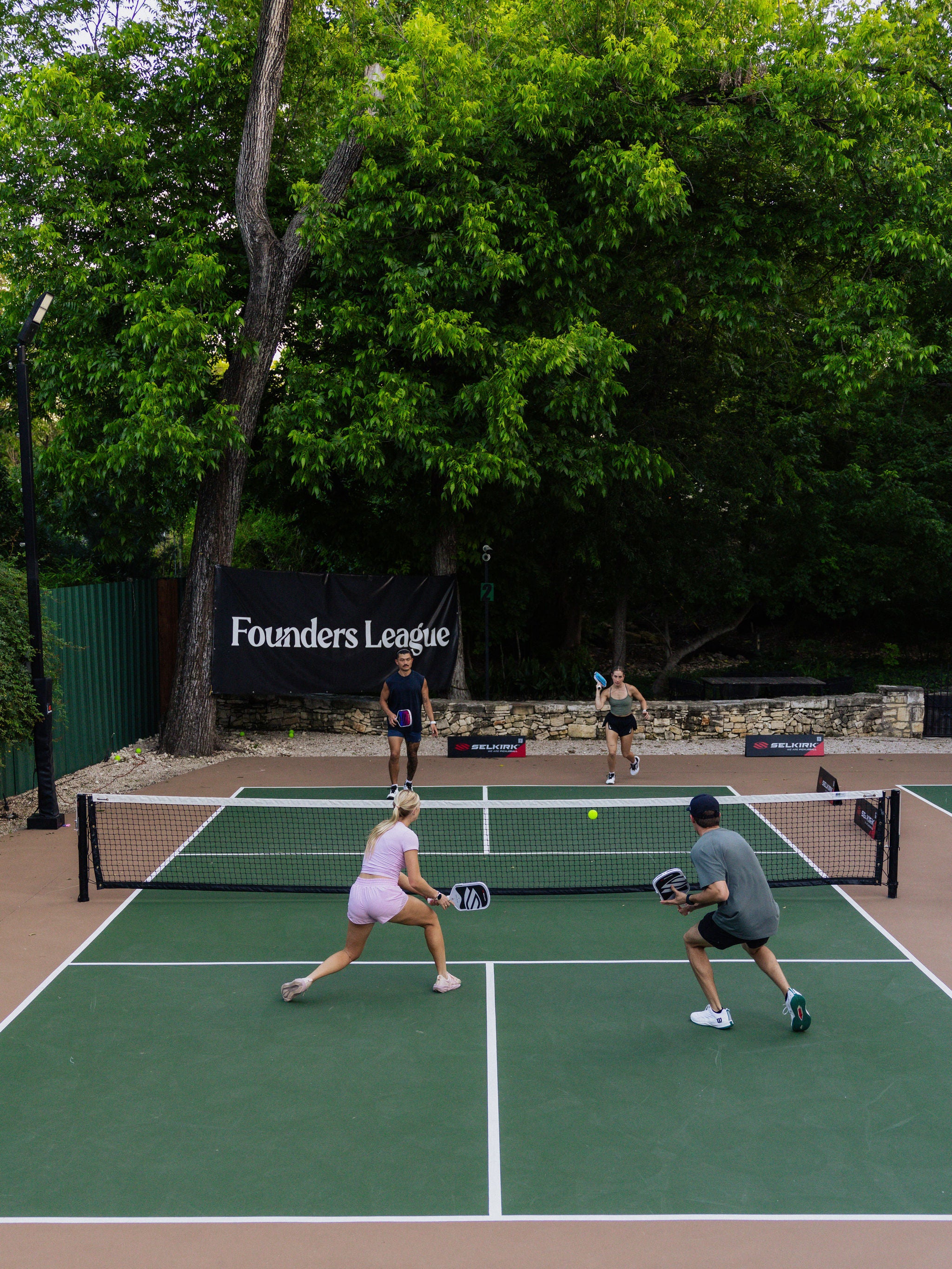 A shot from above shows four players in a pickleball game on an outdoor court. 
