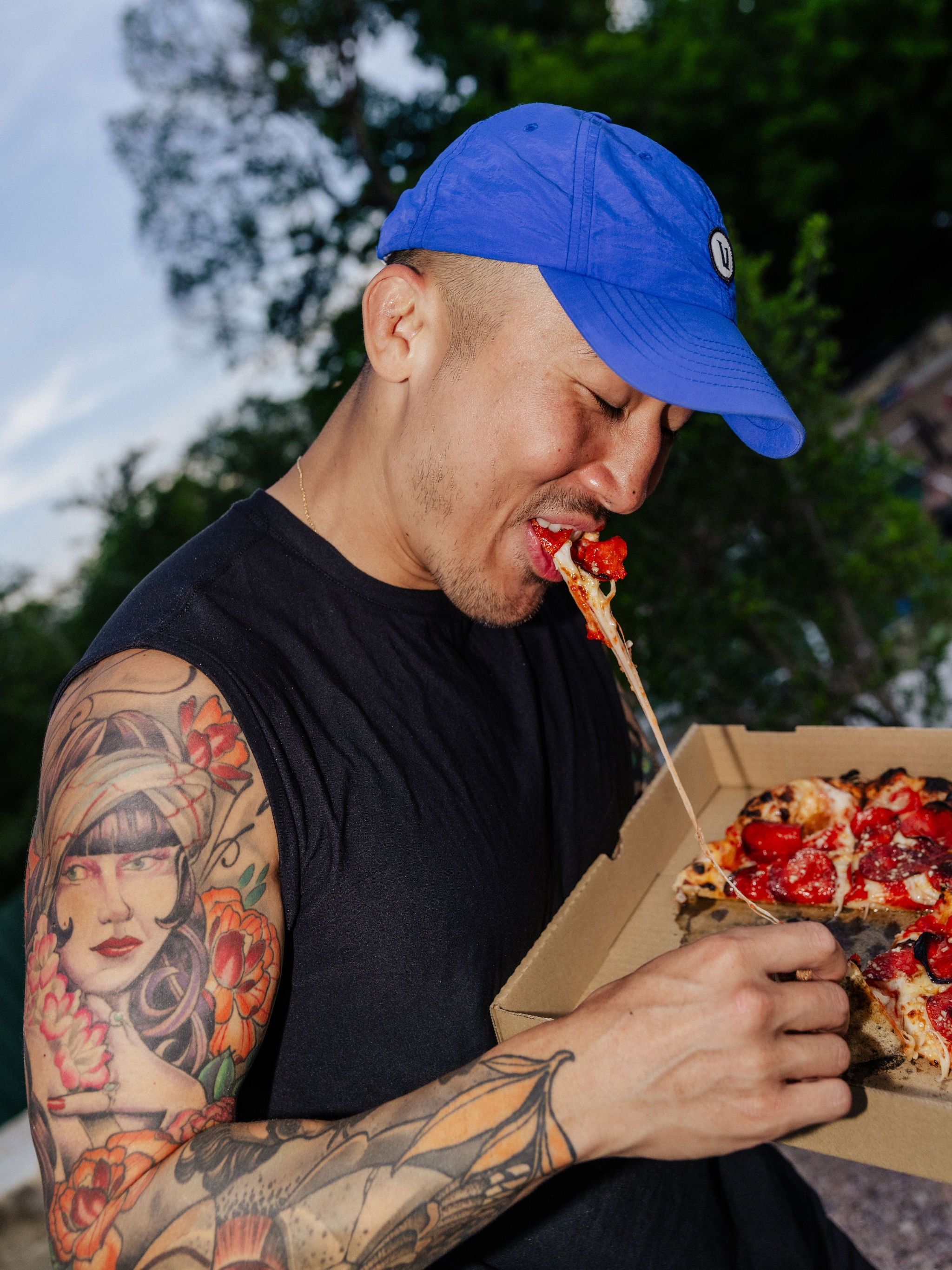 A man pulls a bite of pizza with a long string of cheese. 