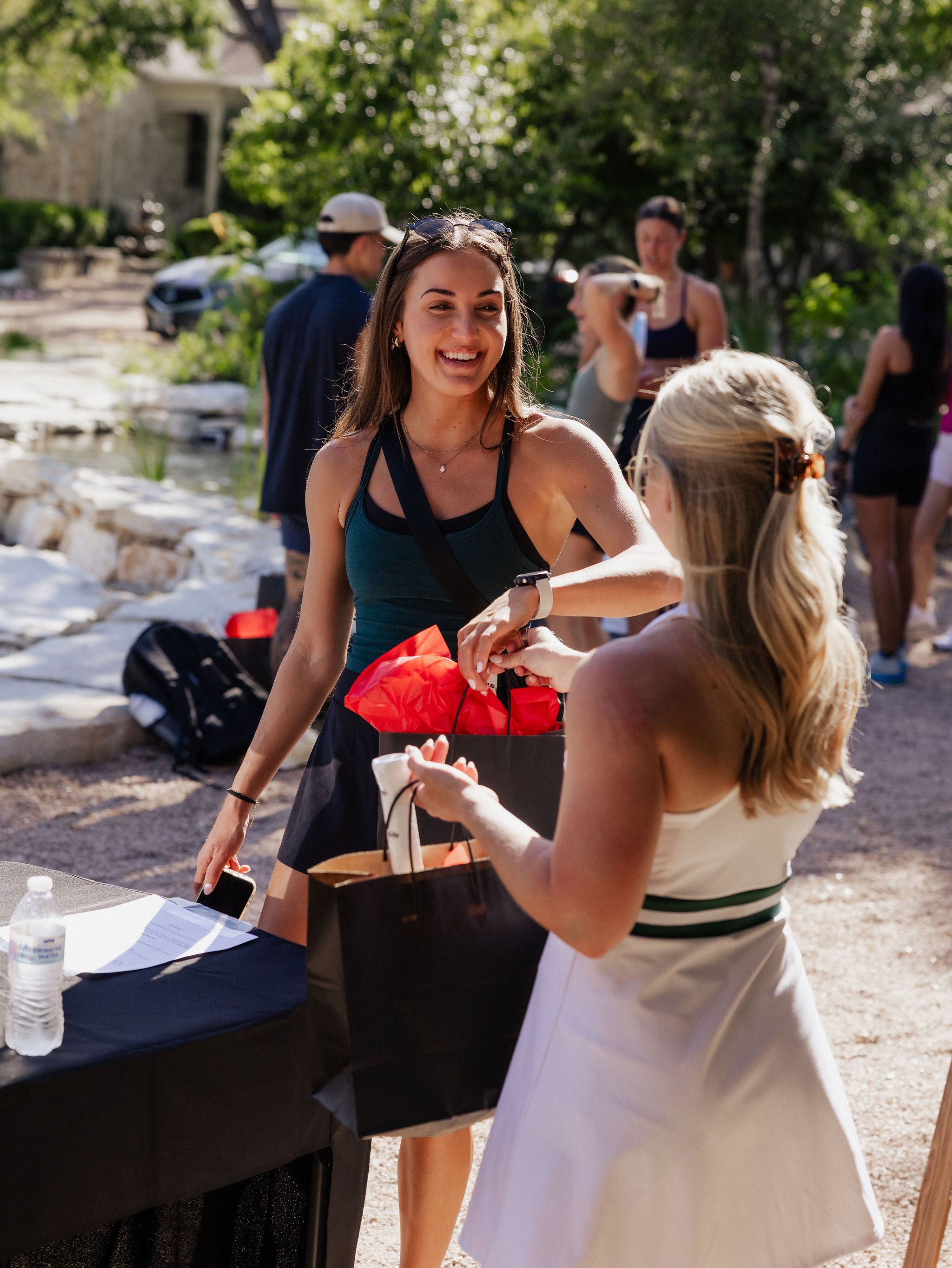 A woman hands another woman a fit bag with pickleball paddles in it. 