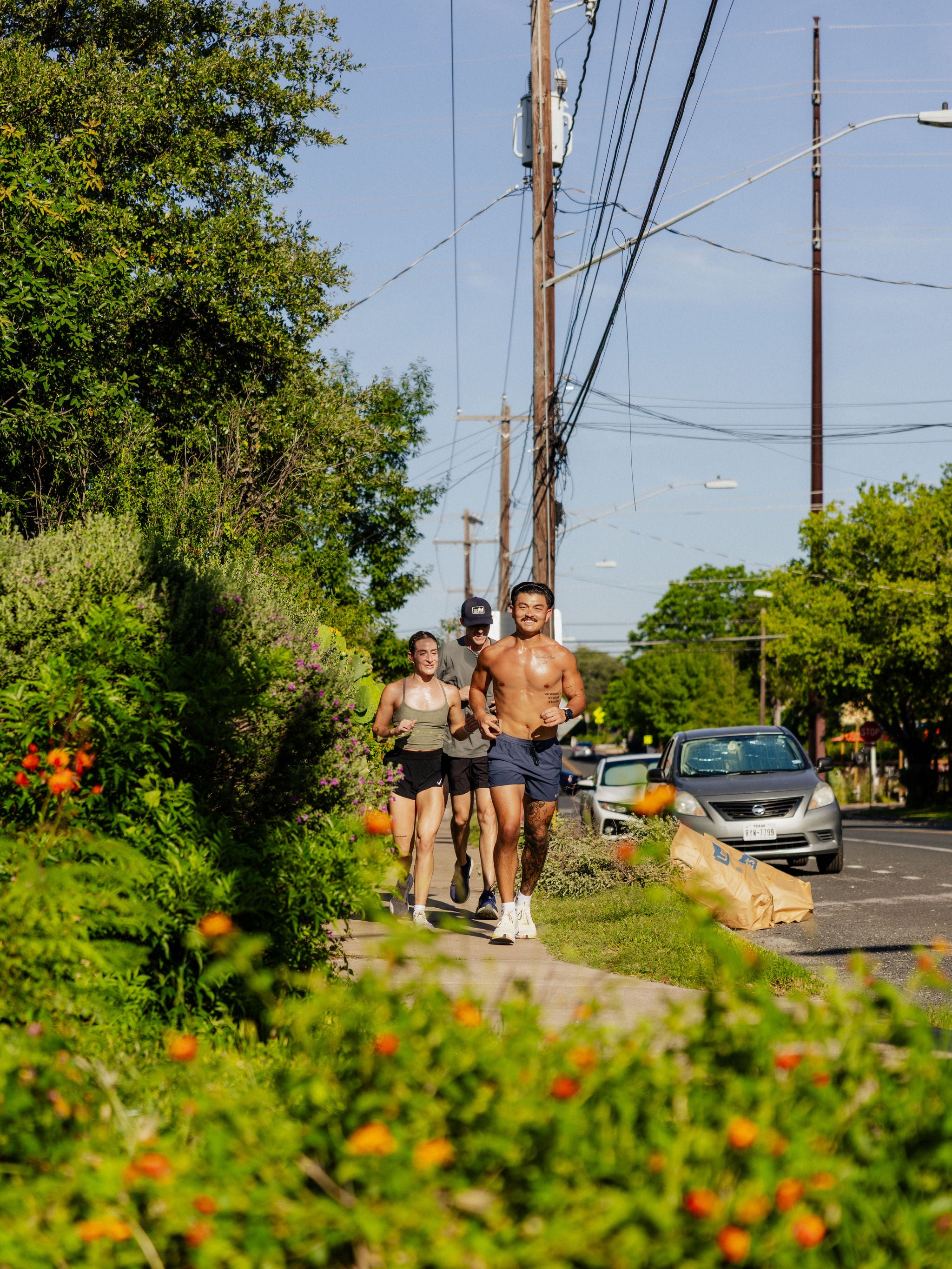An image frames a group of three joggers with plants as they jog alongside a road in Austin. 