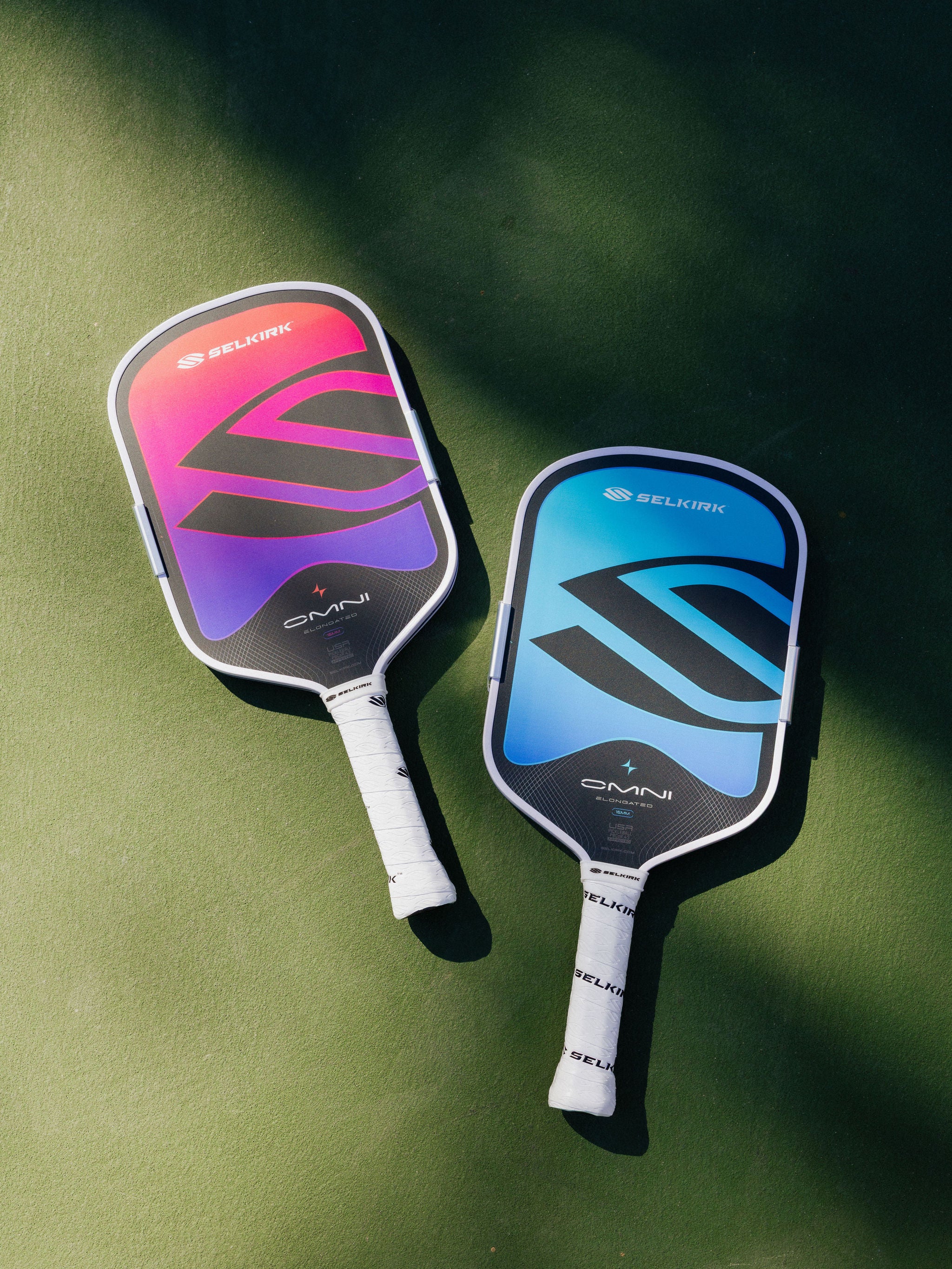Two Selkirk OMNI pickleball paddles lay side-by-side on a pickleball court. 