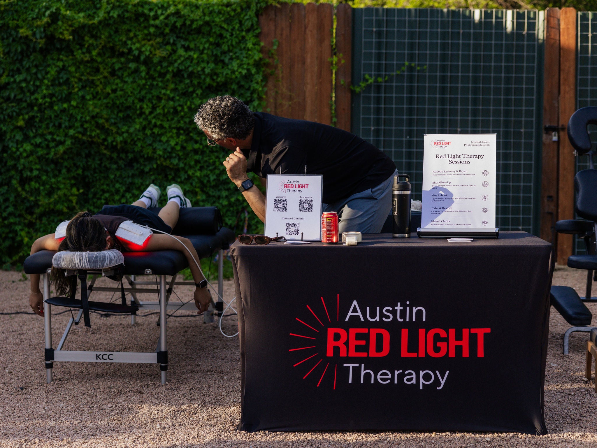 A man runs a red light therapy session for a woman outside. 