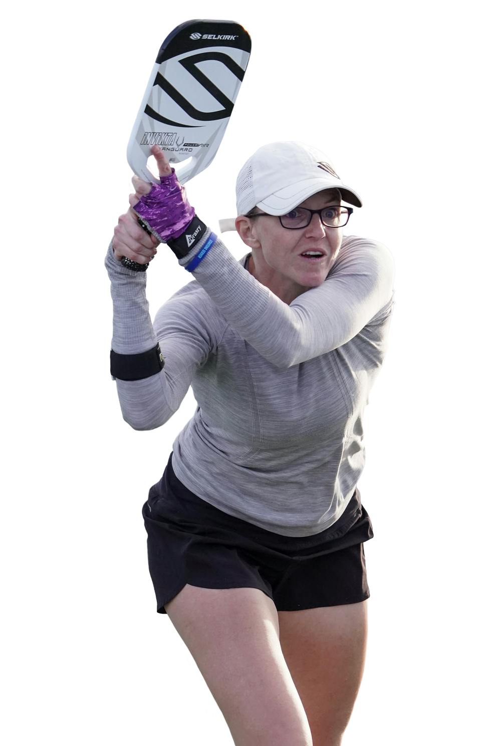 Female pickleball player hitting a two-handed backhand while holding a Selkirk Invikta paddle, wearing a gray long-sleeve top, black skirt, and white cap