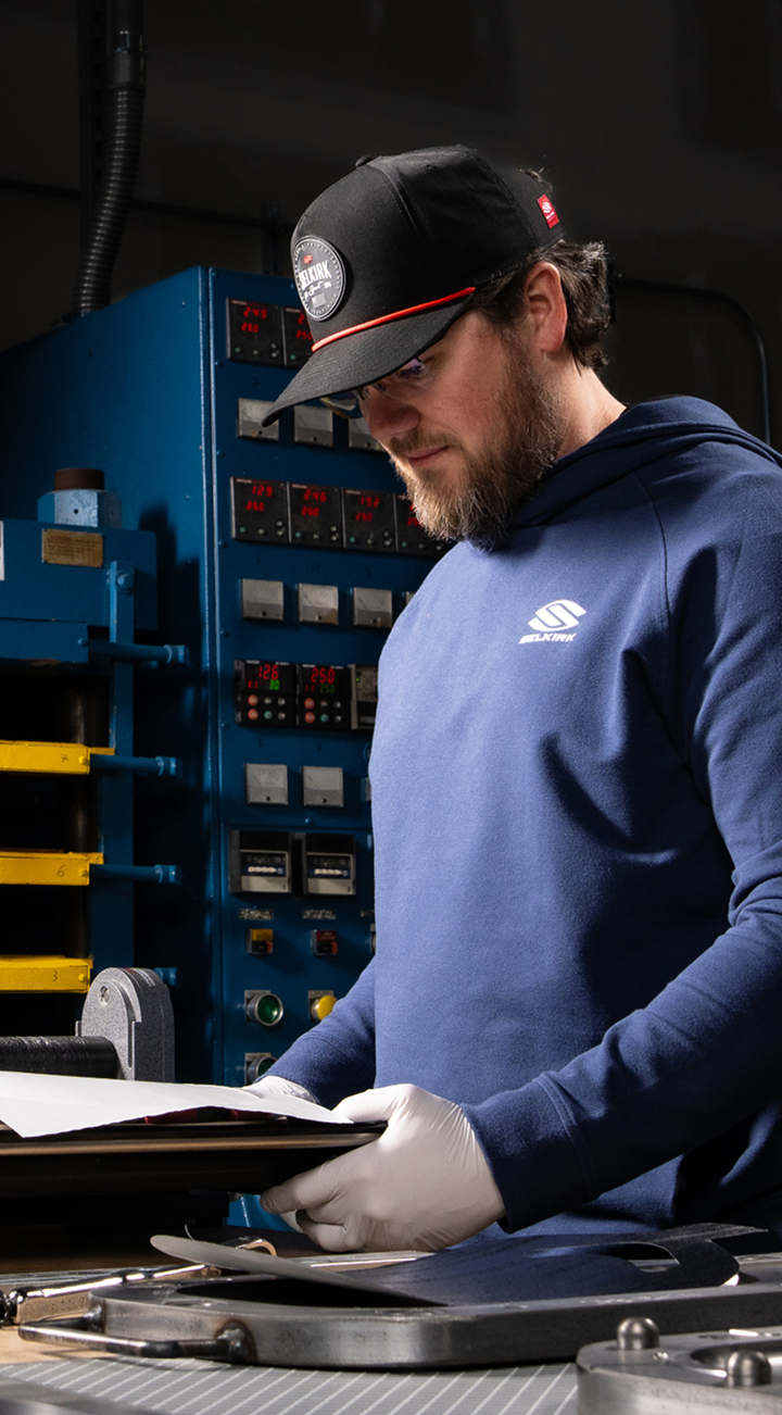 Selkirk Sport engineer operating high-precision manufacturing equipment for pickleball paddle production, wearing branded apparel and cap in a controlled lab environment.