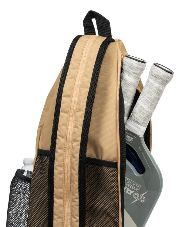 Tan backpack side view holding two pickleball paddles and a water bottle in a mesh pocket.