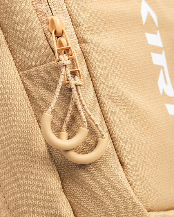Close-up of tan backpack zipper pulls with braided cords and semicircular plastic grips.