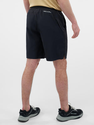 Rear view of person wearing black SELKIRK athletic shorts with elastic waistband and side pockets; matching SELKIRK shoes visible.