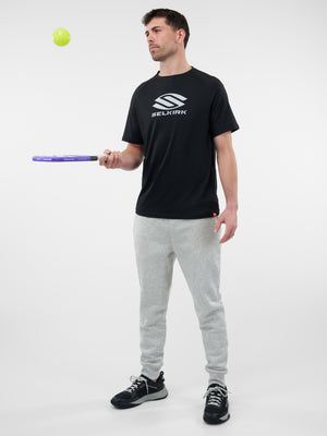 Man balancing a yellow pickleball over a purple paddle while wearing a black shirt with 'SELKIRK' logo.
