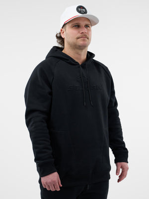 Male model wearing a black hoodie with embossed SELKIRK logo and a white cap with a SELKIRK circular patch