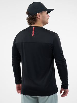 Rear view: man wearing black long-sleeve shirt and cap with vertical red tag reading BERING at upper back.