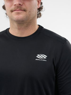 Man wearing black long-sleeve shirt with white SELKIRK logo on left chest; cropped at mouth and shoulders.
