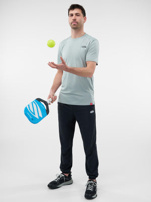 Man balancing a green pickleball on his fingertips while holding a blue pickleball paddle