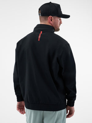 Back view of man wearing a black jacket with a red vertical brand tag at the collar and a black mesh baseball cap.