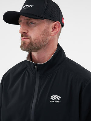 Male model wearing black SELKIRK PICKLEBALL cap and black jacket with SELKIRK logo, looking left