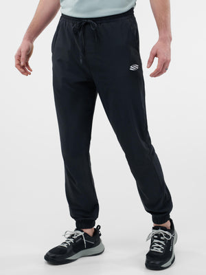 Black jogger pants with elastic cuffs, drawstring waist and small white logo on right thigh, worn with black sneakers.