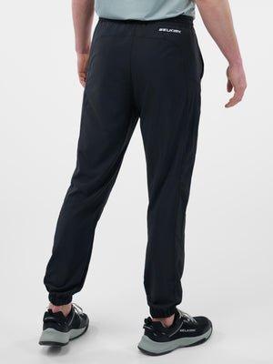 Rear view of person wearing black SELKIRK athletic jogger pants with elastic cuffs and SELKIRK sneakers