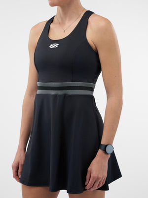 Woman wearing black athletic tennis dress with gray striped waistband and white stylized S logo on chest