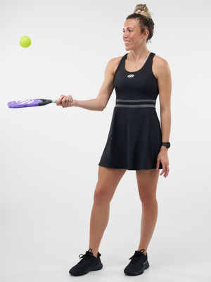 Woman in black athletic dress holding a purple pickleball paddle, bouncing a neon green ball