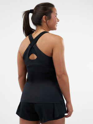 Back view of a woman wearing a black crisscross-back athletic tank and black layered shorts against a white background.