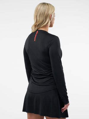 Woman seen from back wearing black long-sleeve athletic top and black skirt, small vertical red logo at upper back.