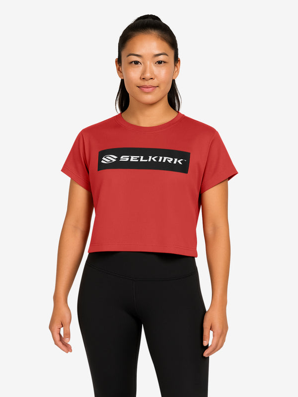 Woman wearing cropped red boxy tee with black SELKIRK logo across the chest